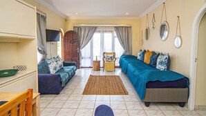 A cozy living room with a sofa, a chair, a dining table, and a large window with curtains. - La Loggia B&B (Umhlanga)