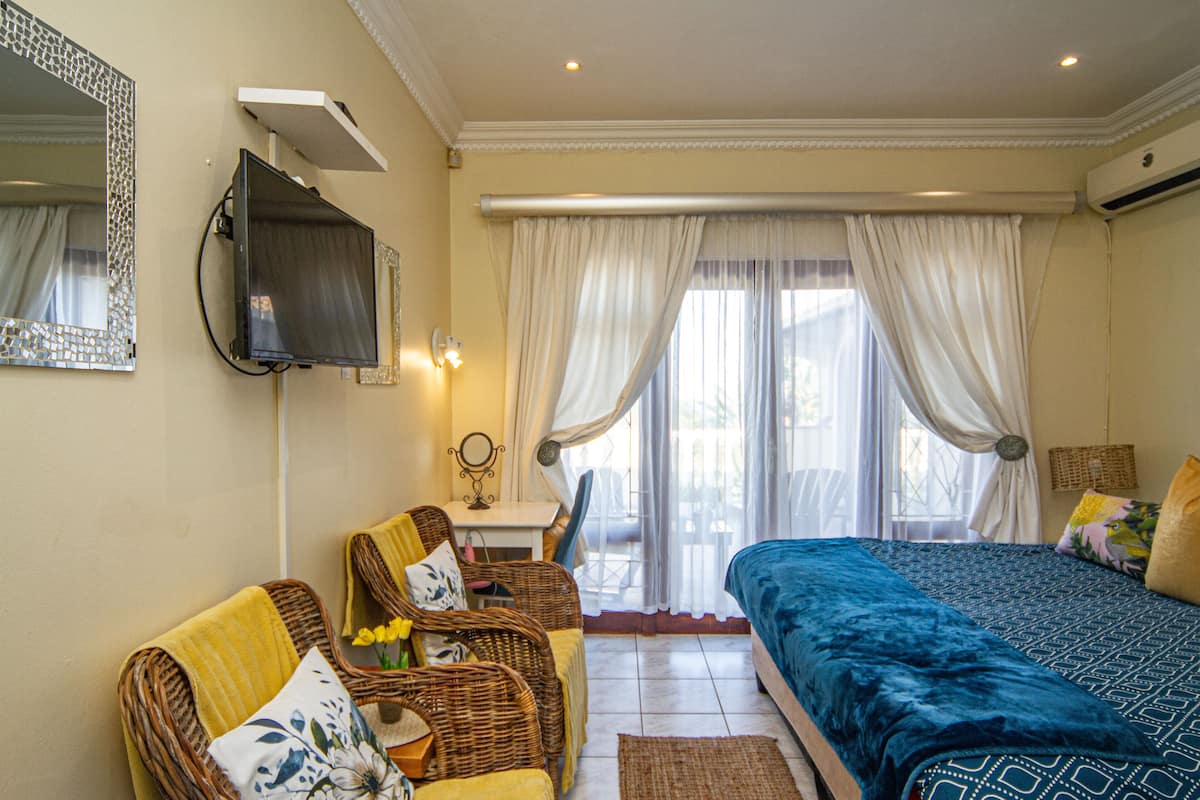 A hotel room with a bed, two wicker chairs, a small table, and a mirror on the wall.