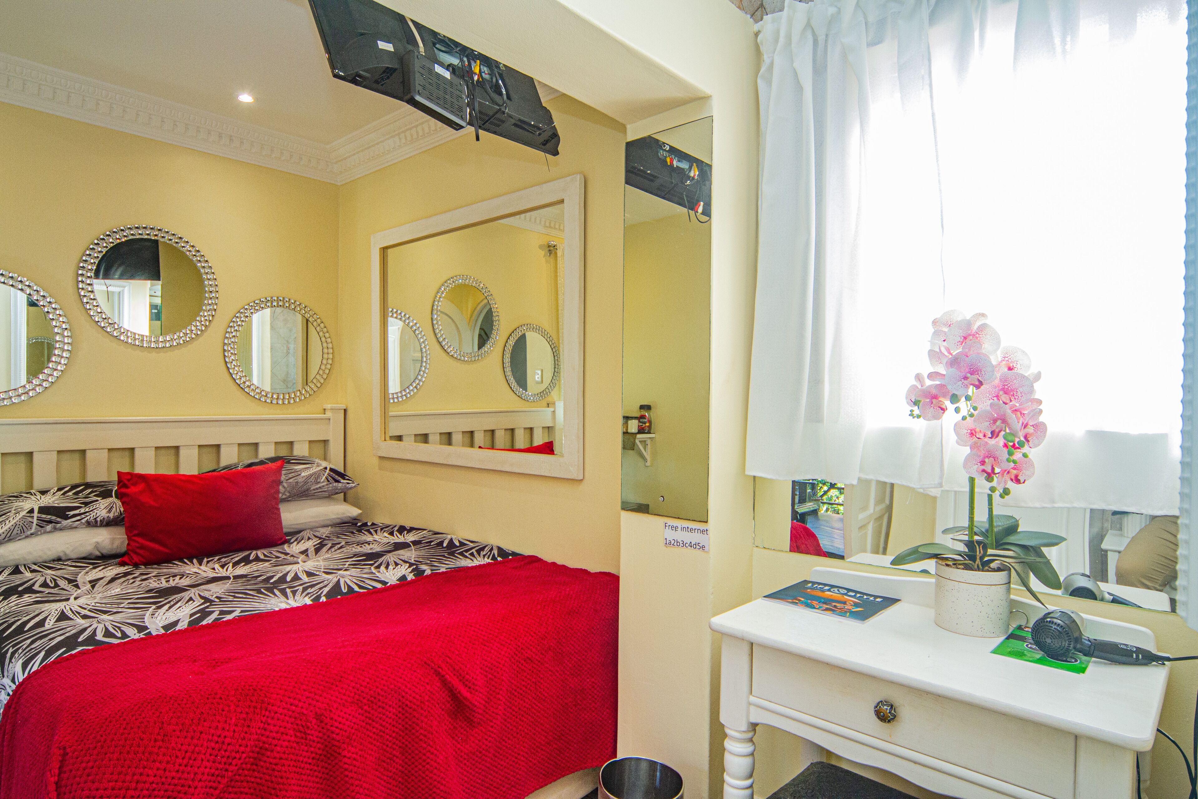 A hotel room with a bed, a desk, a potted orchid, and multiple mirrors on the wall.