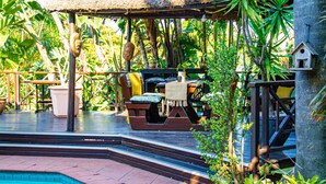 A poolside area with a thatched roof, wooden furniture, and lush tropical plants. - La Loggia B&B (Umhlanga)