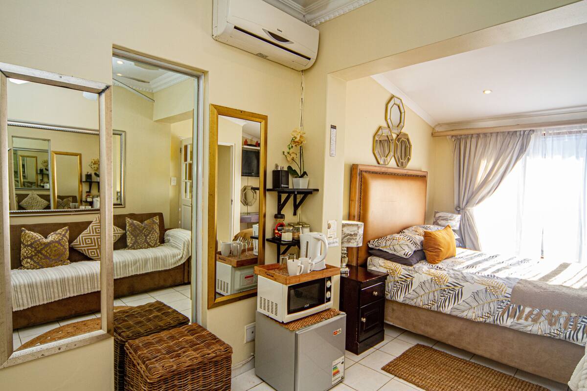 A hotel room with a bed, a microwave, a refrigerator, a mirror, and a window with curtains.