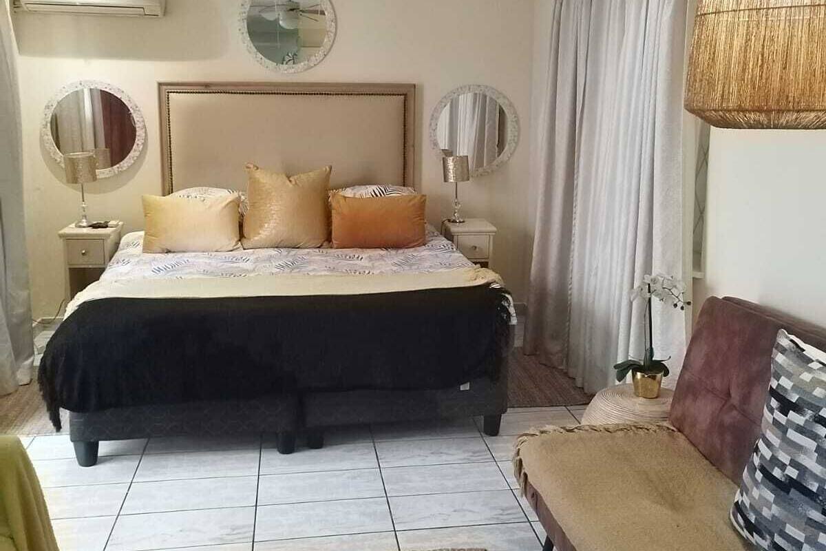 A bedroom with a bed, a sofa, a ceiling fan, and a large mirror.