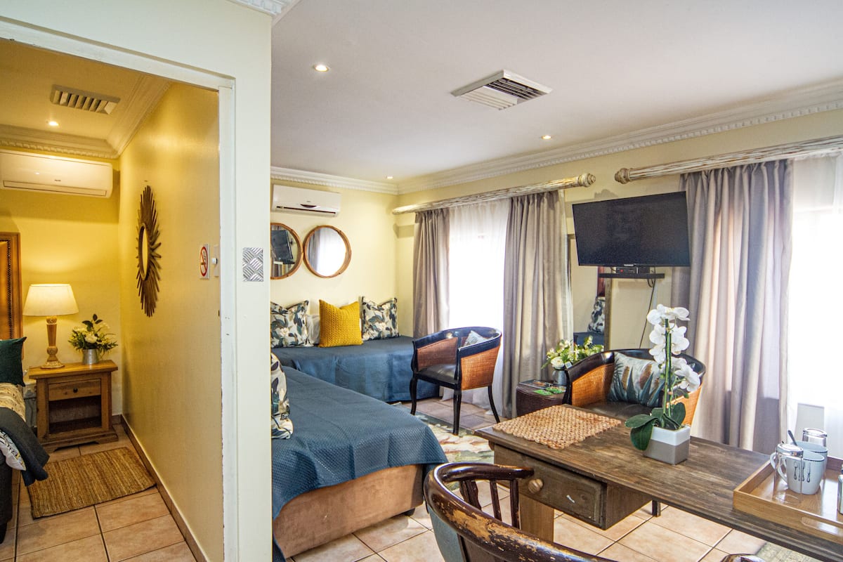 A hotel room with a bed, a sofa, a dining table, and a TV.