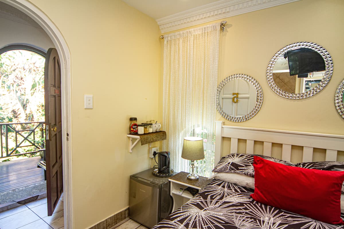 A bedroom with a bed, a nightstand, a lamp, a mirror, and a window with curtains.