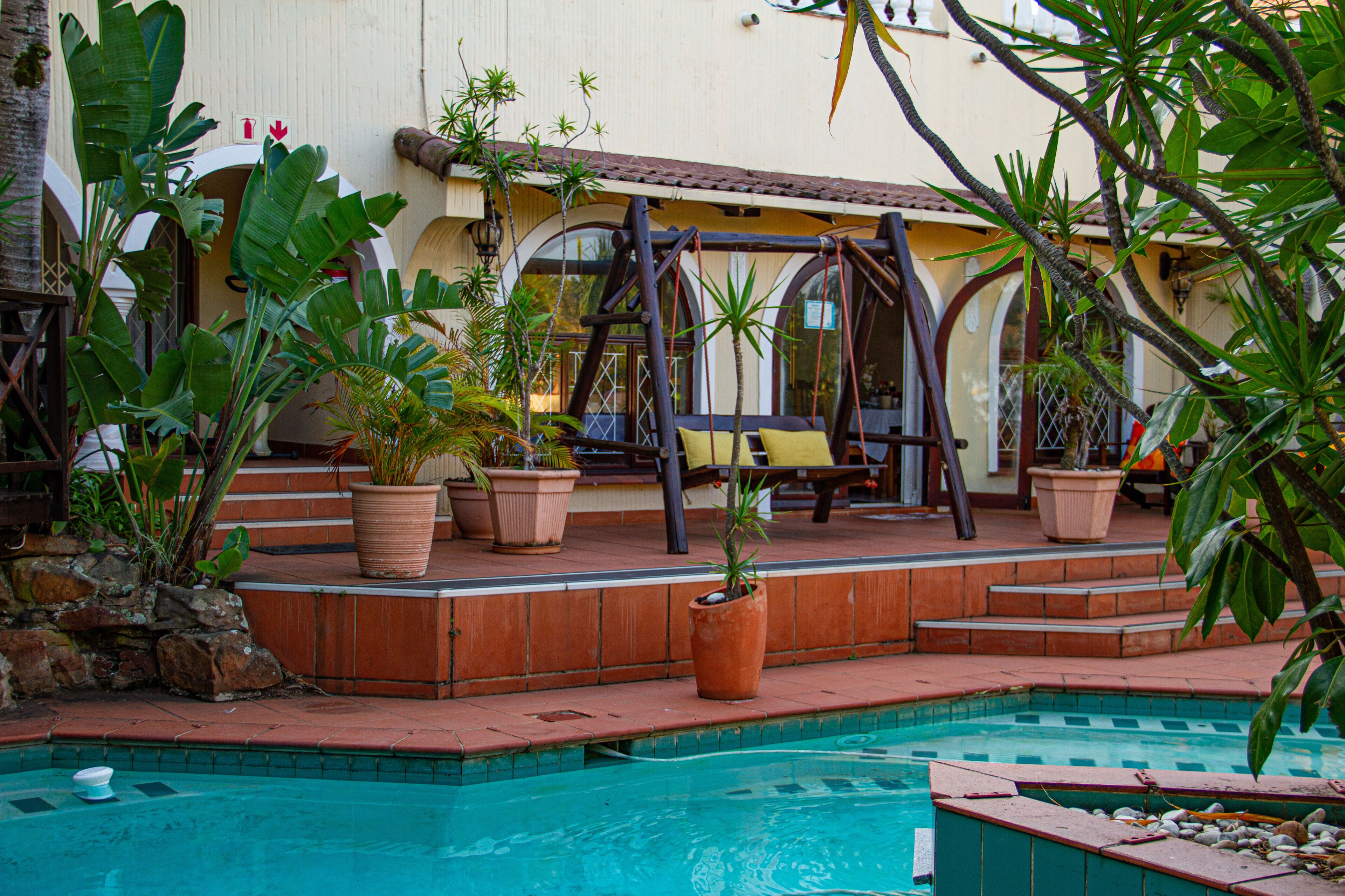 Un espace piscine doté d’une terrasse en bois, de plantes en pot et d’une balançoire.