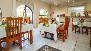 A dining area with wooden chairs and tables, a tiled floor, and a view through an arched window. - La Loggia B&B (Umhlanga)