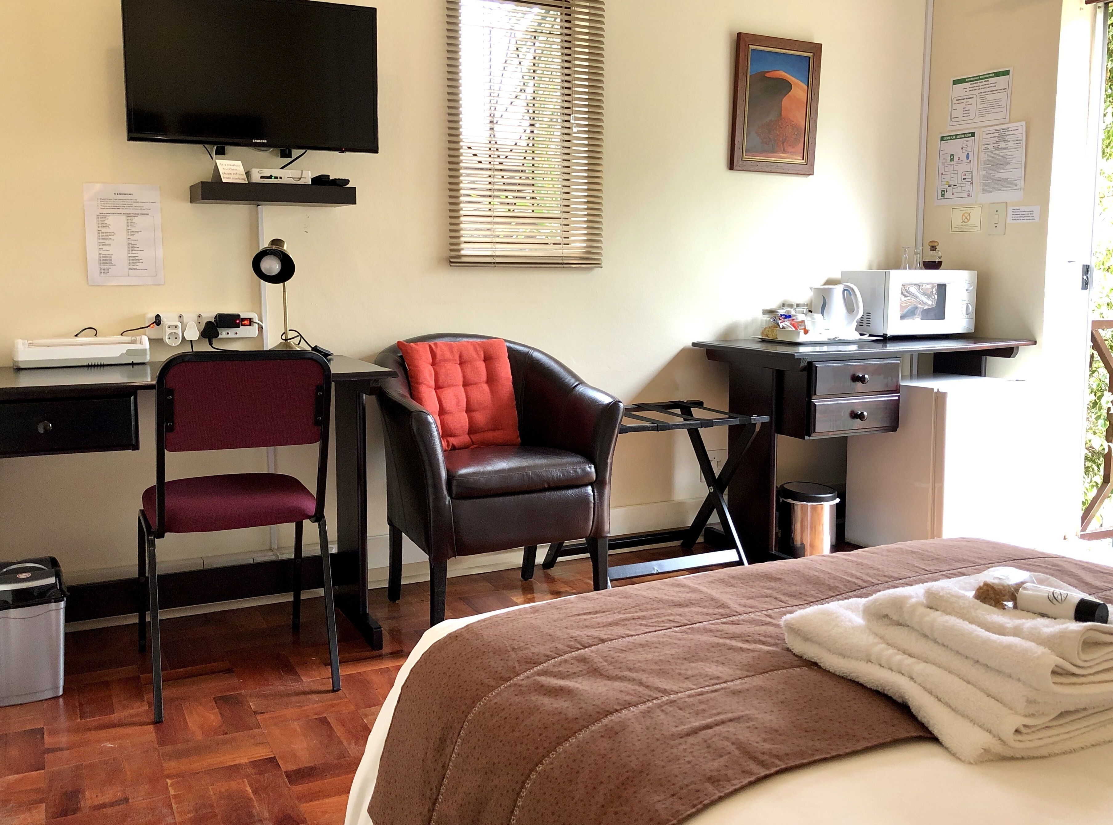 Ein Hotelzimmer mit einem Bett, einem Schreibtisch mit Computer, einem Sessel, einem Fernseher und einem Fenster mit Jalousien.