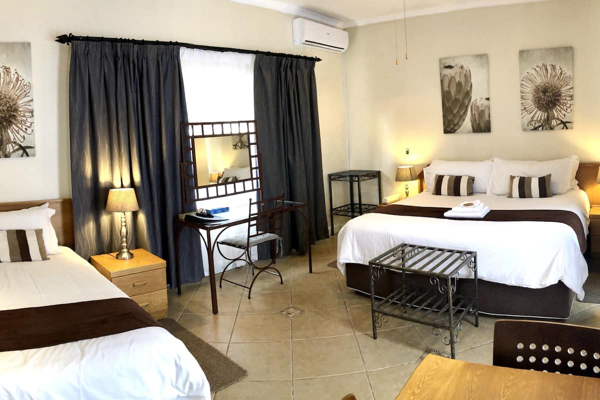 Ein Hotelzimmer mit zwei Betten, einem Schreibtisch, einem Stuhl, einem kleinen Tisch und Bildern an der Wand.