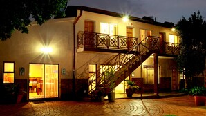 A two-story building with a balcony, a staircase, and potted plants.