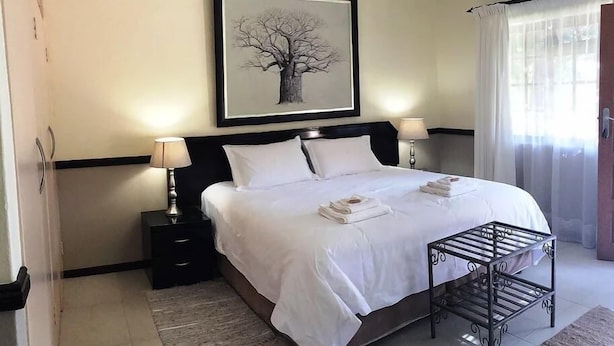 A hotel room with a large bed, two bedside tables with lamps, a framed picture on the wall, and a window with curtains.