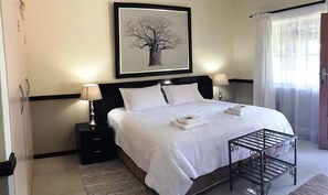 Ein Hotelzimmer mit einem großen Bett, zwei Nachttischen mit Lampen, einem gerahmten Bild an der Wand und einem Fenster mit Vorhängen.