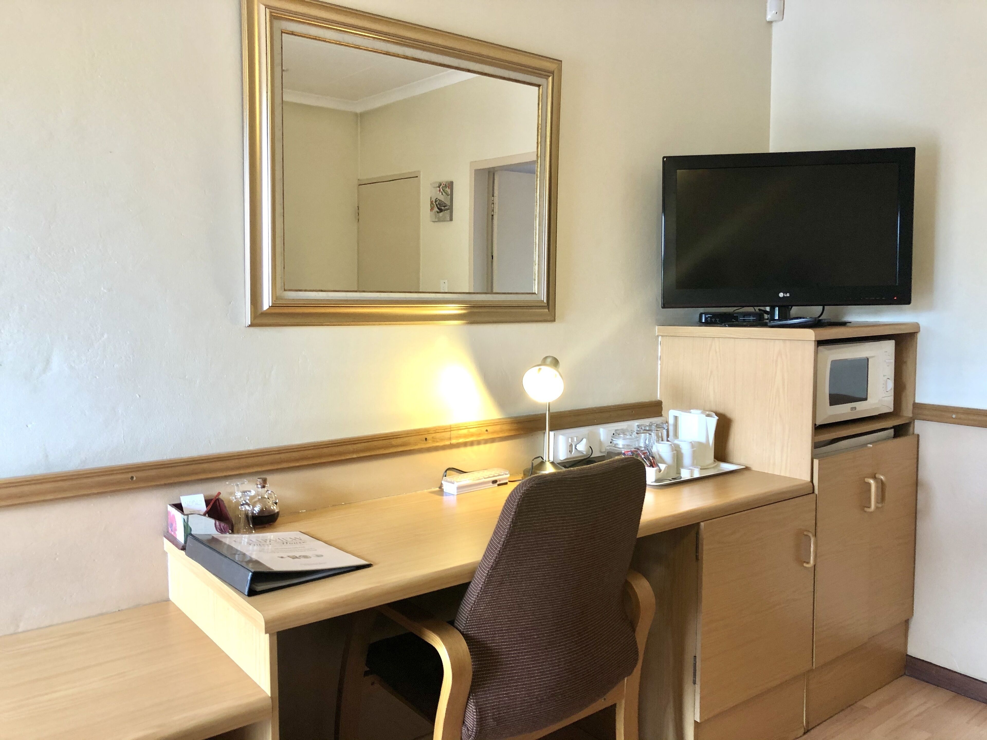 A hotel room with a wooden desk, a chair, a television, a microwave, and a cabinet.