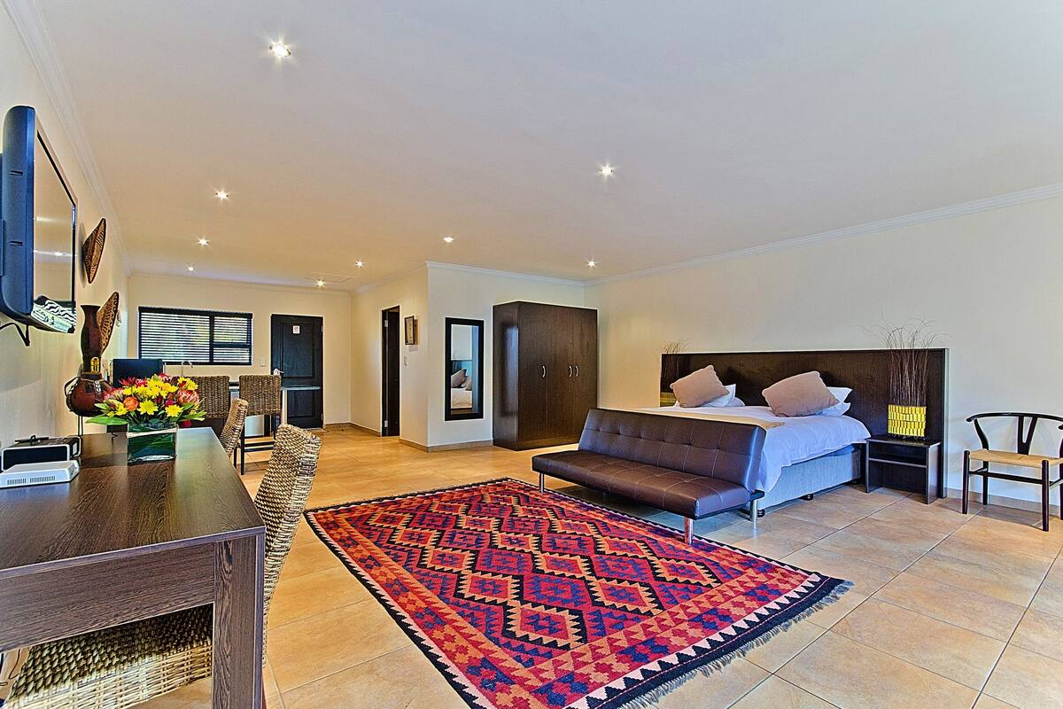 Ein modernes Schlafzimmer mit einem großen Bett, einer Couch, einem Fernseher und einem Essbereich mit Tisch und Stühlen.