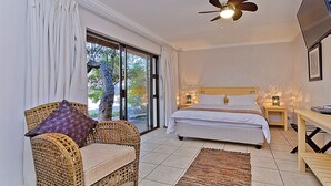 Une chambre à coucher avec un lit, une chaise en osier, un ventilateur de plafond et un téléviseur.