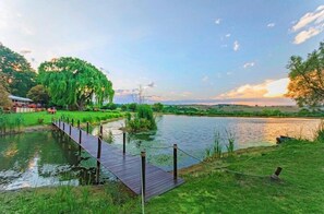 A wooden deck over a calm river, surrounded by lush greenery and trees. - Stornoway Lodge (Muldersdrift)