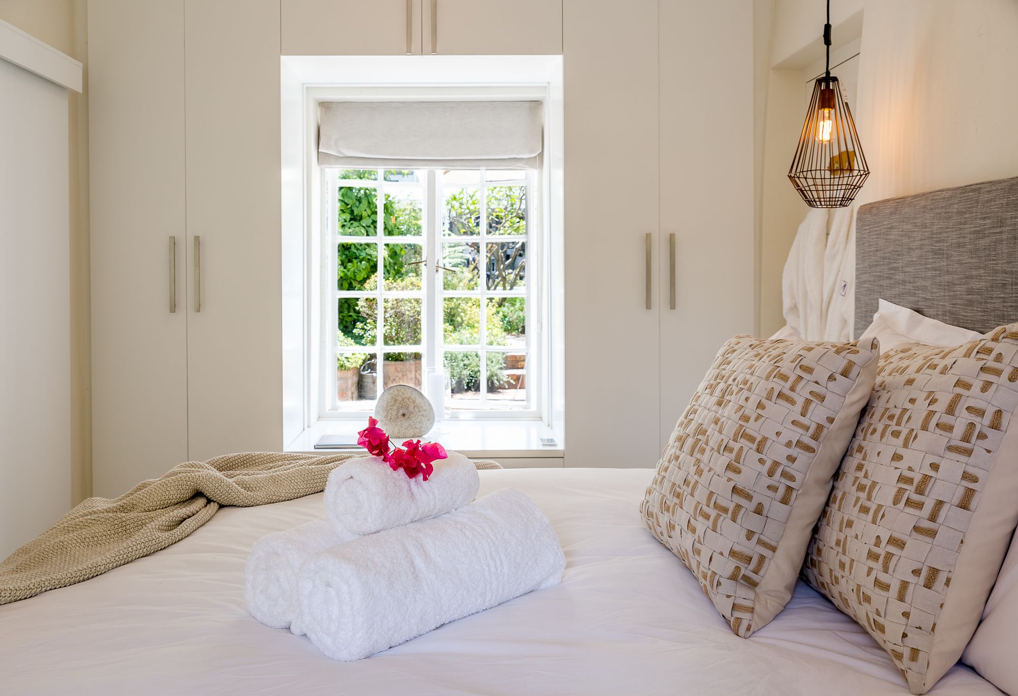 Une chambre à coucher avec un lit, une fenêtre donnant sur un paysage verdoyant et un luminaire suspendu.