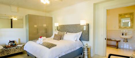 A well-lit bedroom with a large bed, bedside tables, a wardrobe, and a bathroom visible through an open door.