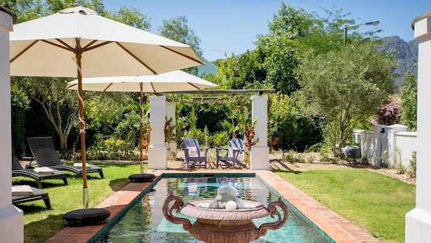 A pool area with a fountain, lounge chairs, and umbrellas. - Macaron Boutique Guest House (Franschhoek)