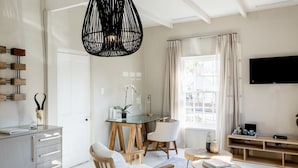 A modern living room with a glass desk, wooden chairs, a sofa, and a TV mounted on the wall. - Macaron Boutique Guest House (Franschhoek)
