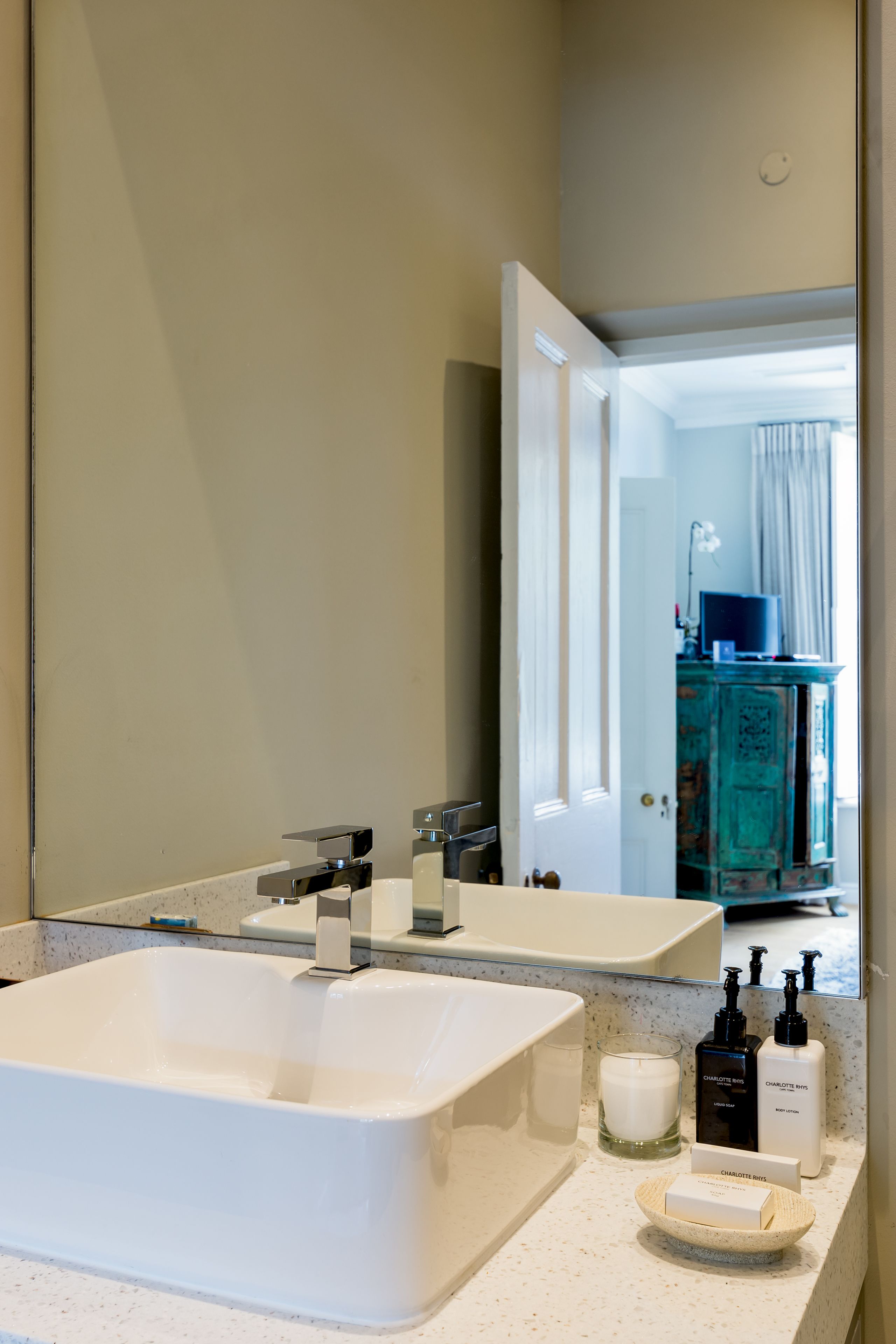 A bathroom with a large white sink, a mirror, and toiletries on the counter.