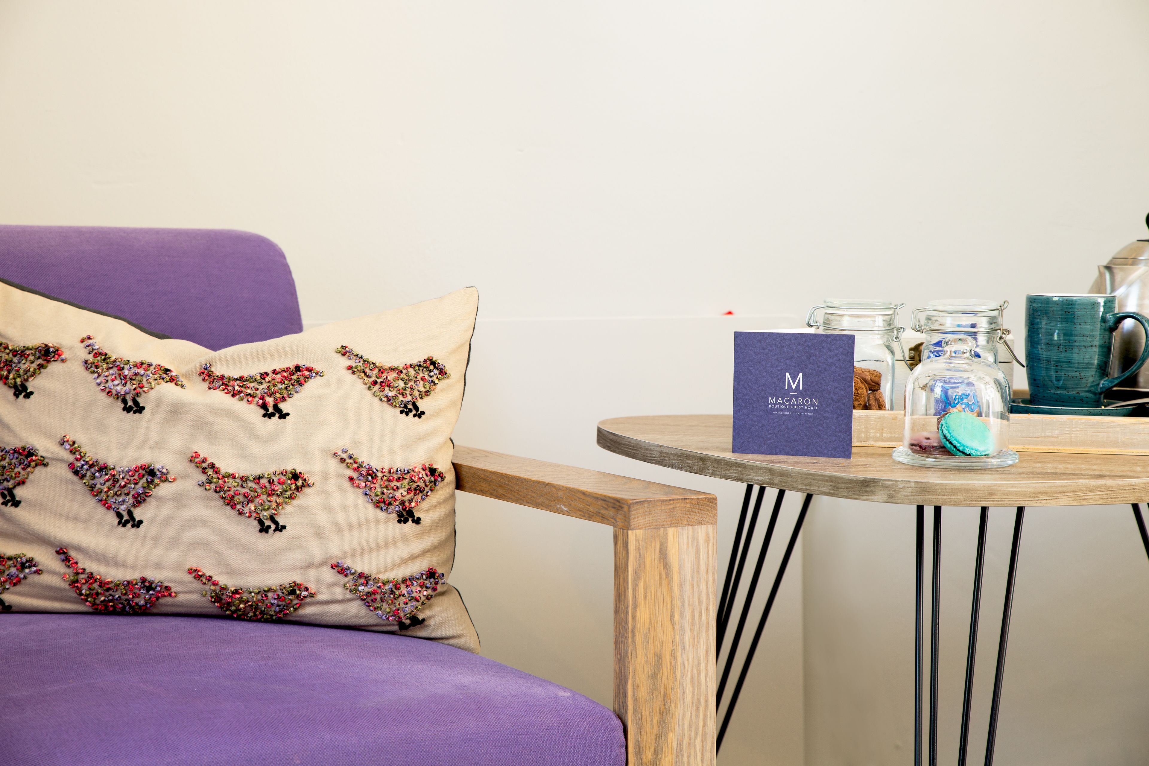 Un canapé violet agrémenté d’un coussin décoratif, une petite table ronde en bois sur laquelle est posée une carte, un bocal en verre et une tasse bleue.