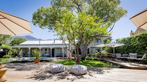 A wooden deck with outdoor seating, a pool, and a large tree in the center. - Macaron Boutique Guest House (Franschhoek)
