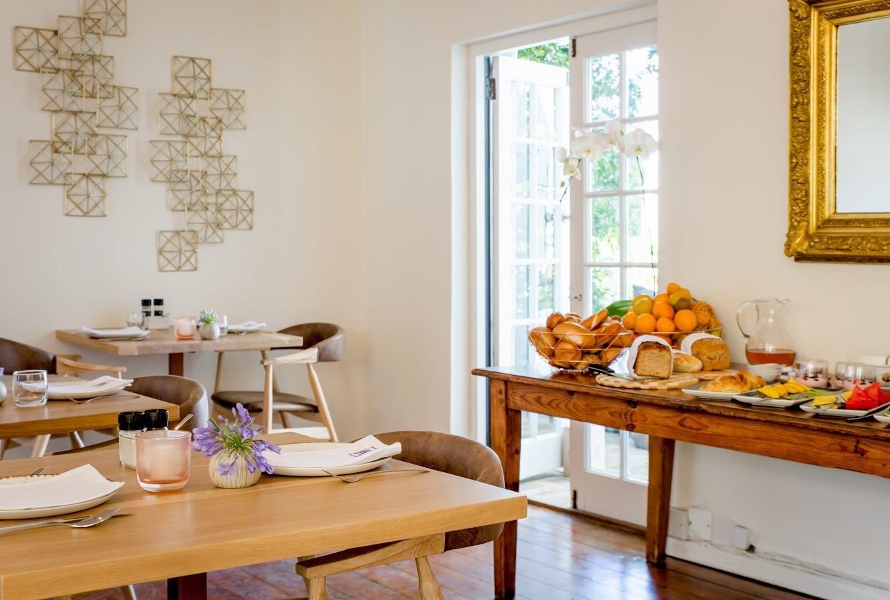 Un coin repas avec une table en bois mise pour le petit-déjeuner, une fenêtre offrant une belle vue et un élément décoratif mural.