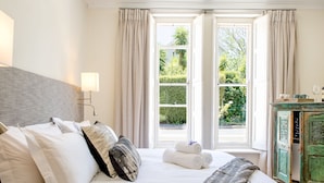 A hotel room with a large bed, a nightstand, a lamp, and a view of greenery through a window. - Macaron Boutique Guest House (Franschhoek)