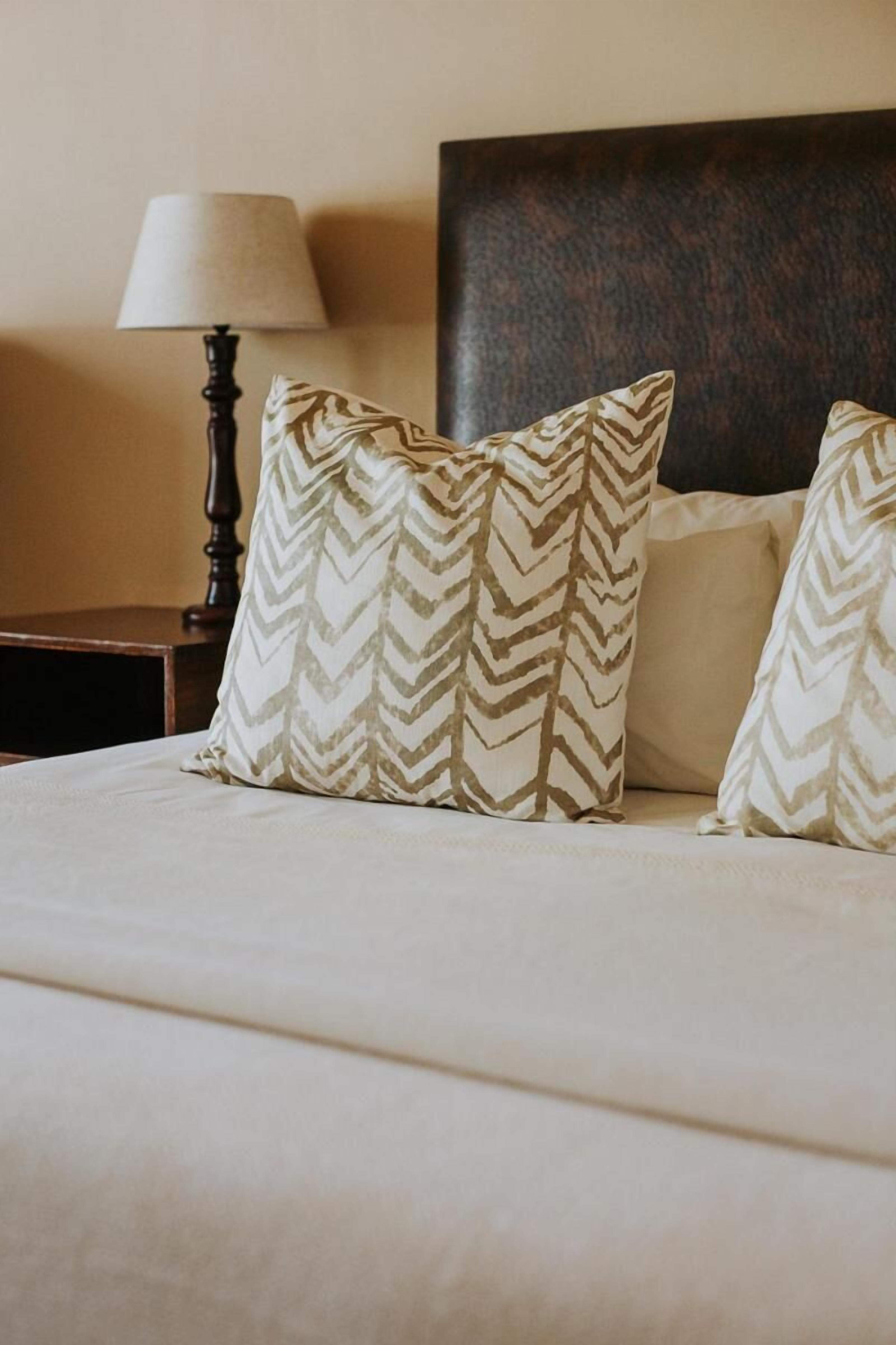 Una cama bien hecha con dos almohadones estampados y un cabecero oscuro.