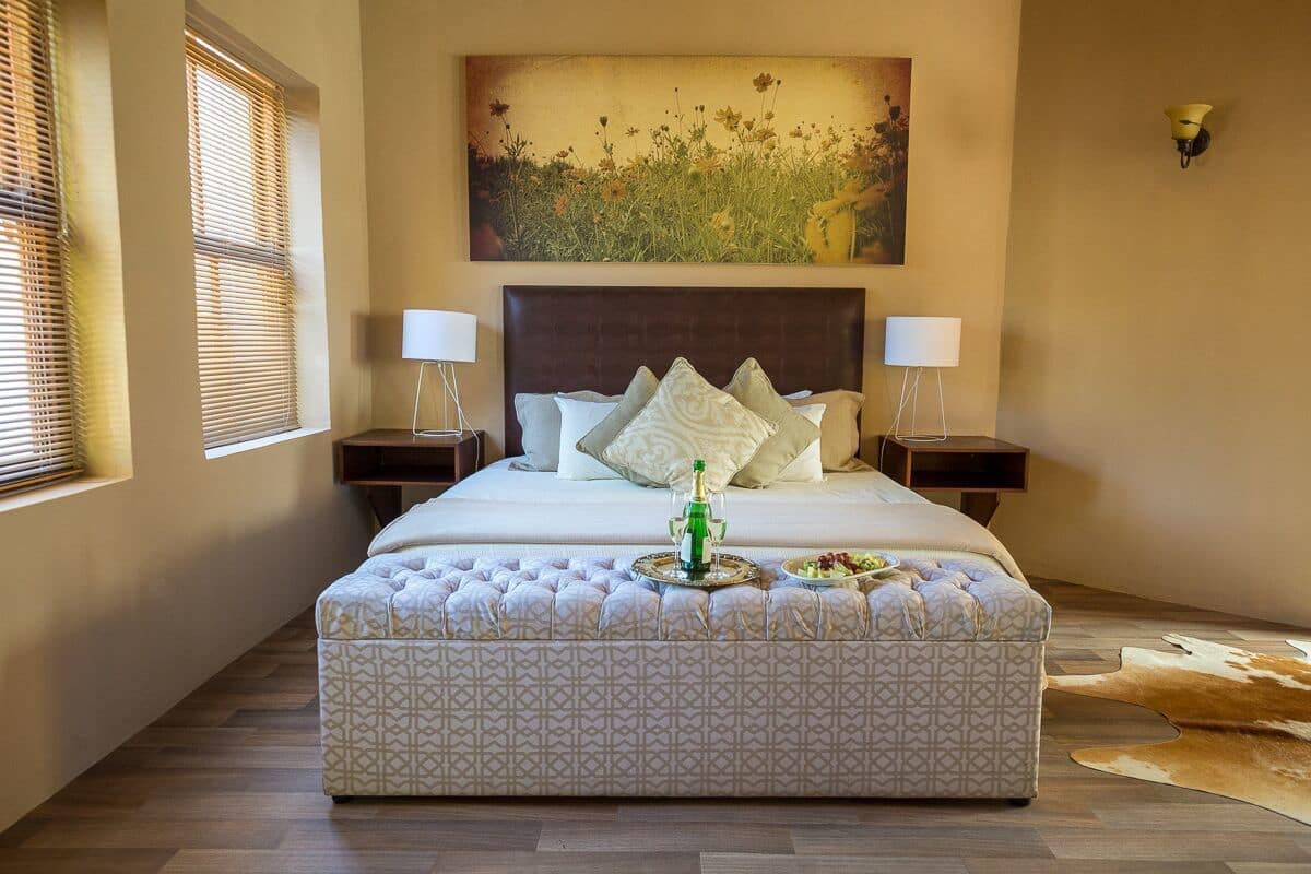 A neatly arranged bedroom with a large bed, two bedside tables with lamps, a decorative wall piece, and a patterned ottoman.
