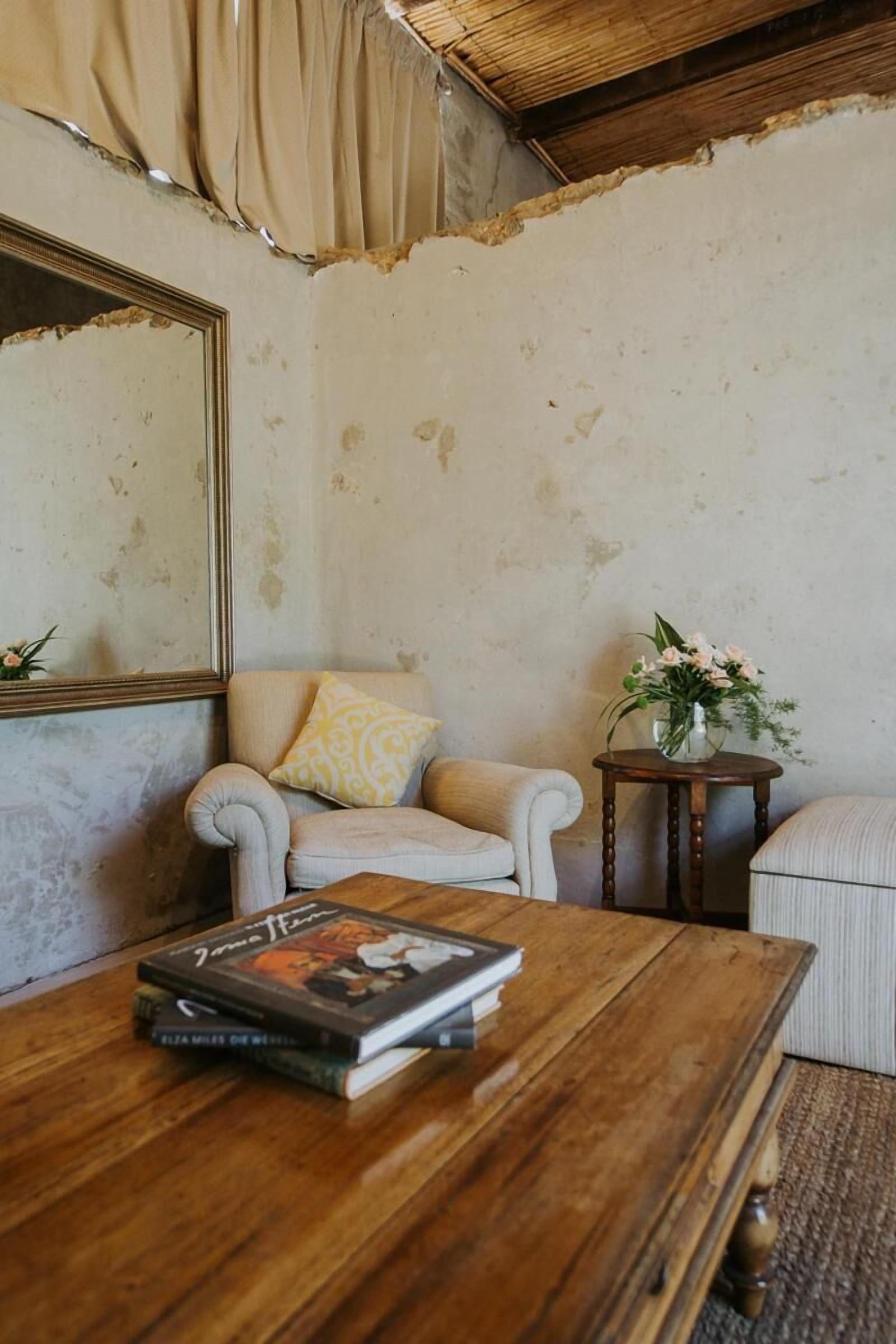 Una habitación con una mesa de centro de madera, una silla con cojín, una mesita auxiliar con un florero y un espejo grande en la pared.