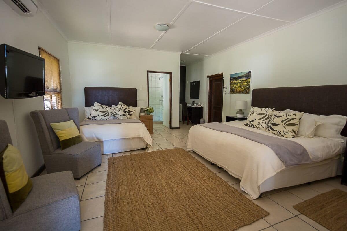A hotel room with two beds, a TV, a sofa, and a bathroom visible through an open door.