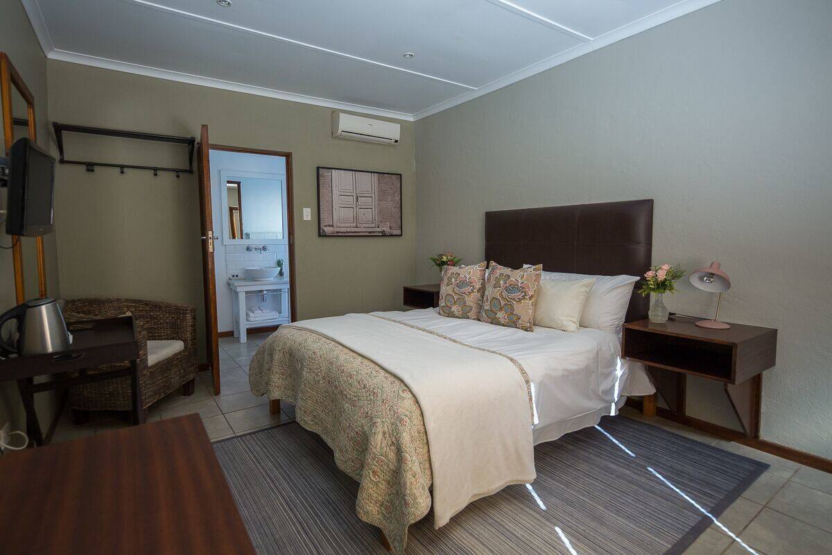 A bedroom with a bed, bedside tables, a chair, a desk, and a bathroom visible through an open door.