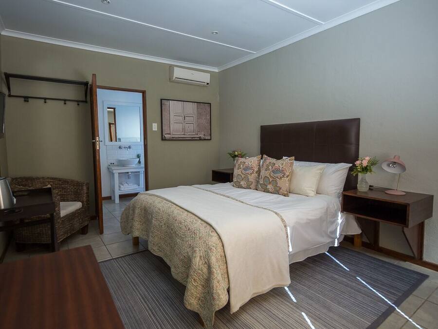Un dormitorio con cama, mesitas de noche, una silla, un escritorio y un baño visible a través de una puerta abierta.