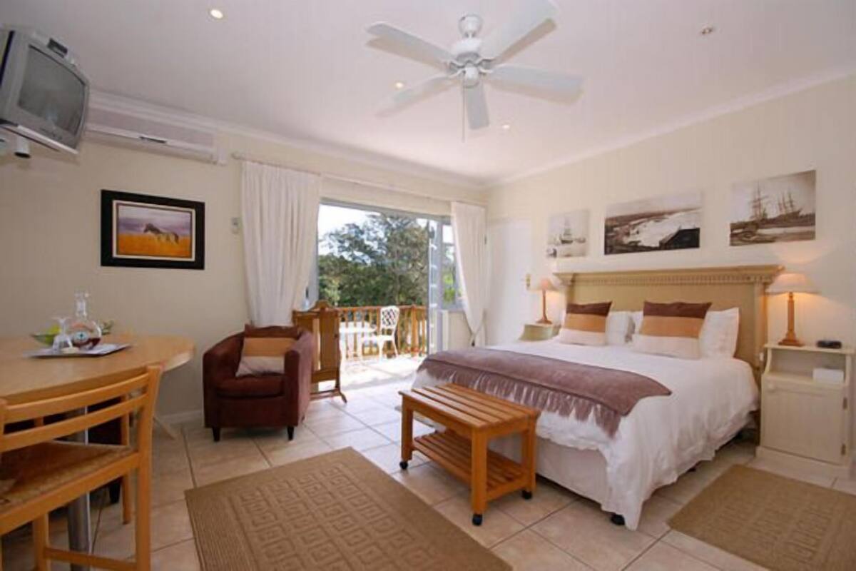 A bedroom with a bed, a desk, a chair, a television, and a balcony.