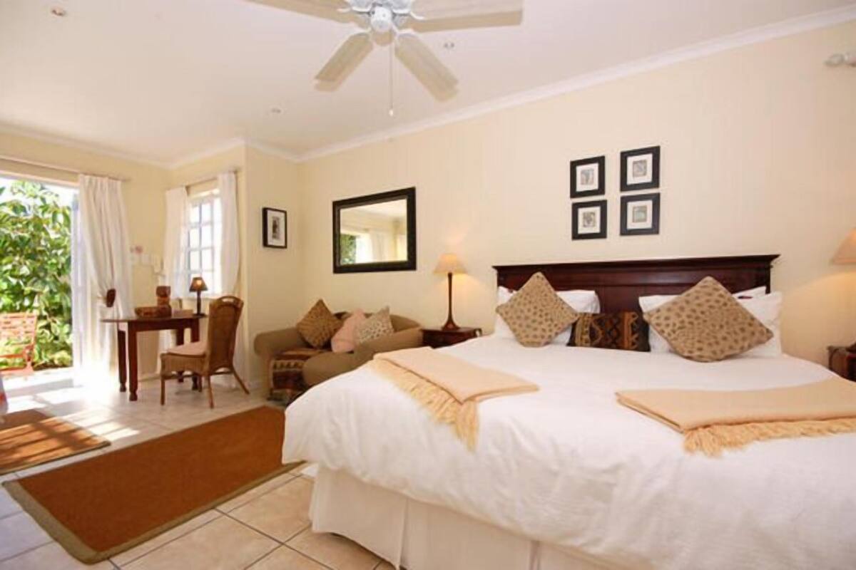 A hotel room with a large bed, two bedside tables, a ceiling fan, and a view of greenery outside.