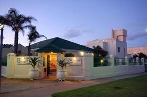 Guests enter through a charming entrance surrounded by lush greenery and palm trees.