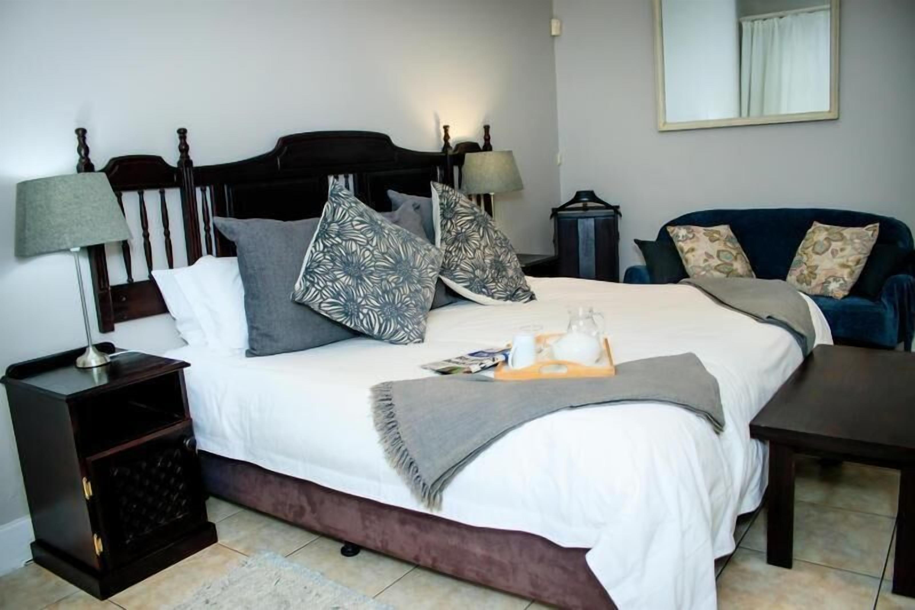 Une chambre à coucher bien rangée, avec un grand lit, une table de chevet, une lampe de lecture, une chaise et un miroir accroché au mur.