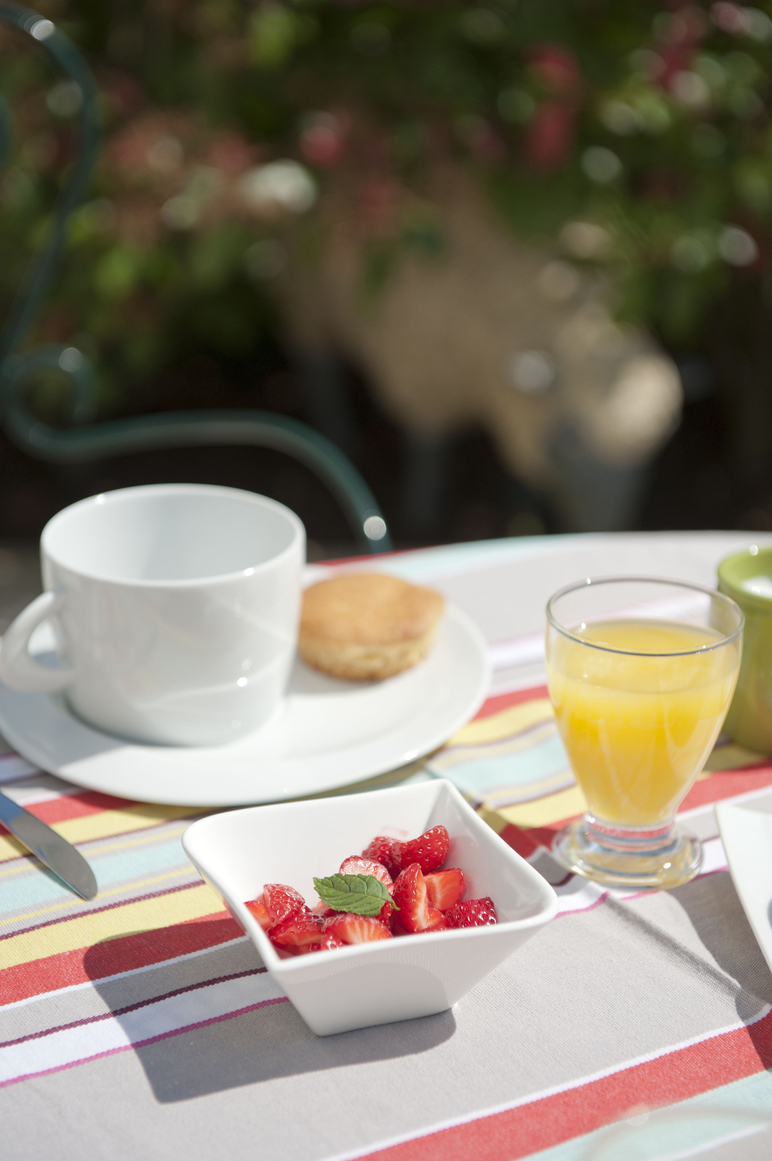 Un desayuno con una taza, un vaso de zumo de naranja, un plato con una galleta y un bol de fresas.