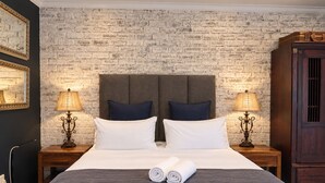 Een hotelkamer met een bakstenen muur, een groot bed met witte lakens, twee nachtkastjes met lampen en een houten garderobe.