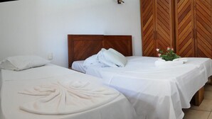Ein Hotelzimmer mit zwei Betten, jeweils mit Holz Kopfteilen und weißen Laken. Im Hintergrund steht ein Holzschrank mit Rautenmuster.