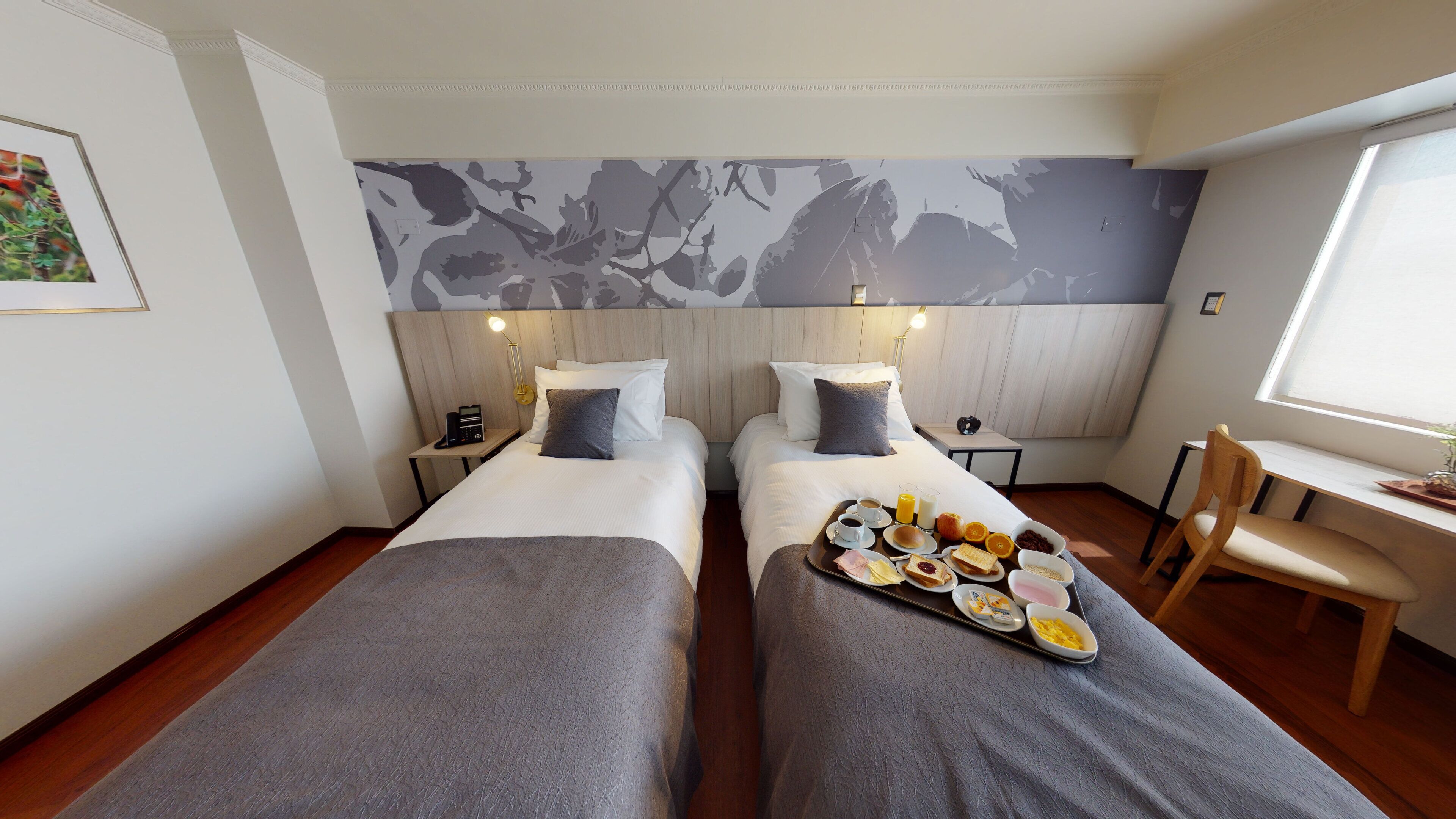 Habitación de hotel con dos camas, un escritorio y una bandeja de desayuno con diversas opciones de comida.
