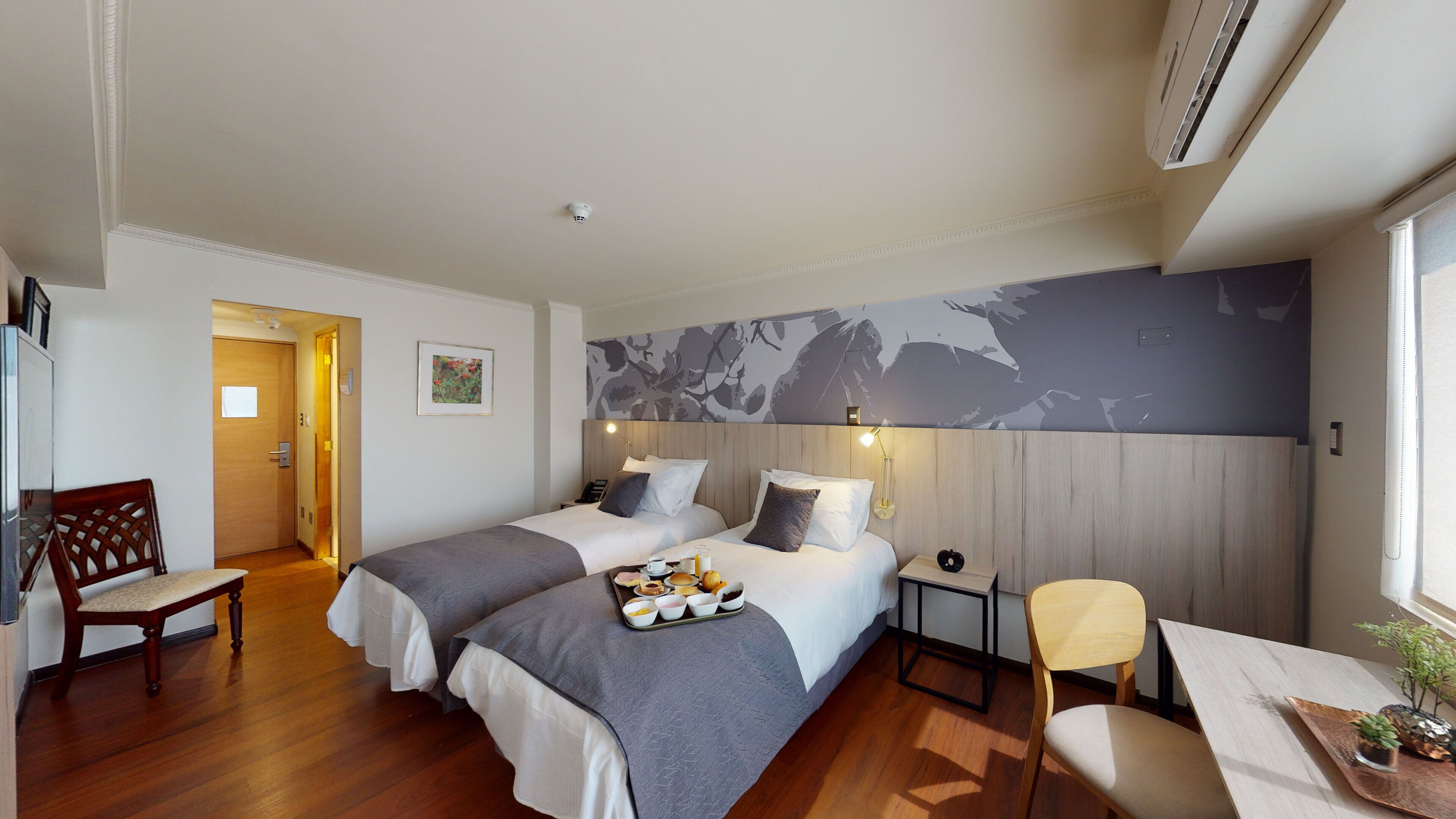 Habitación de hotel con dos camas, piso de madera, un escritorio con silla y un mural grande en la pared.
