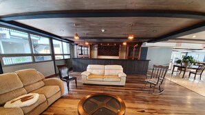 Un amplio salón con piso de madera, un sofá beige y un sofá de cuero blanco, junto a una mesa de centro redonda.