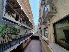 Un estrecho pasillo con balcones, unidades de aire acondicionado y piso de baldosas.