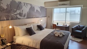 Habitación de hotel con una cama grande, lámparas de noche, un escritorio, una silla y vista al agua por la ventana.