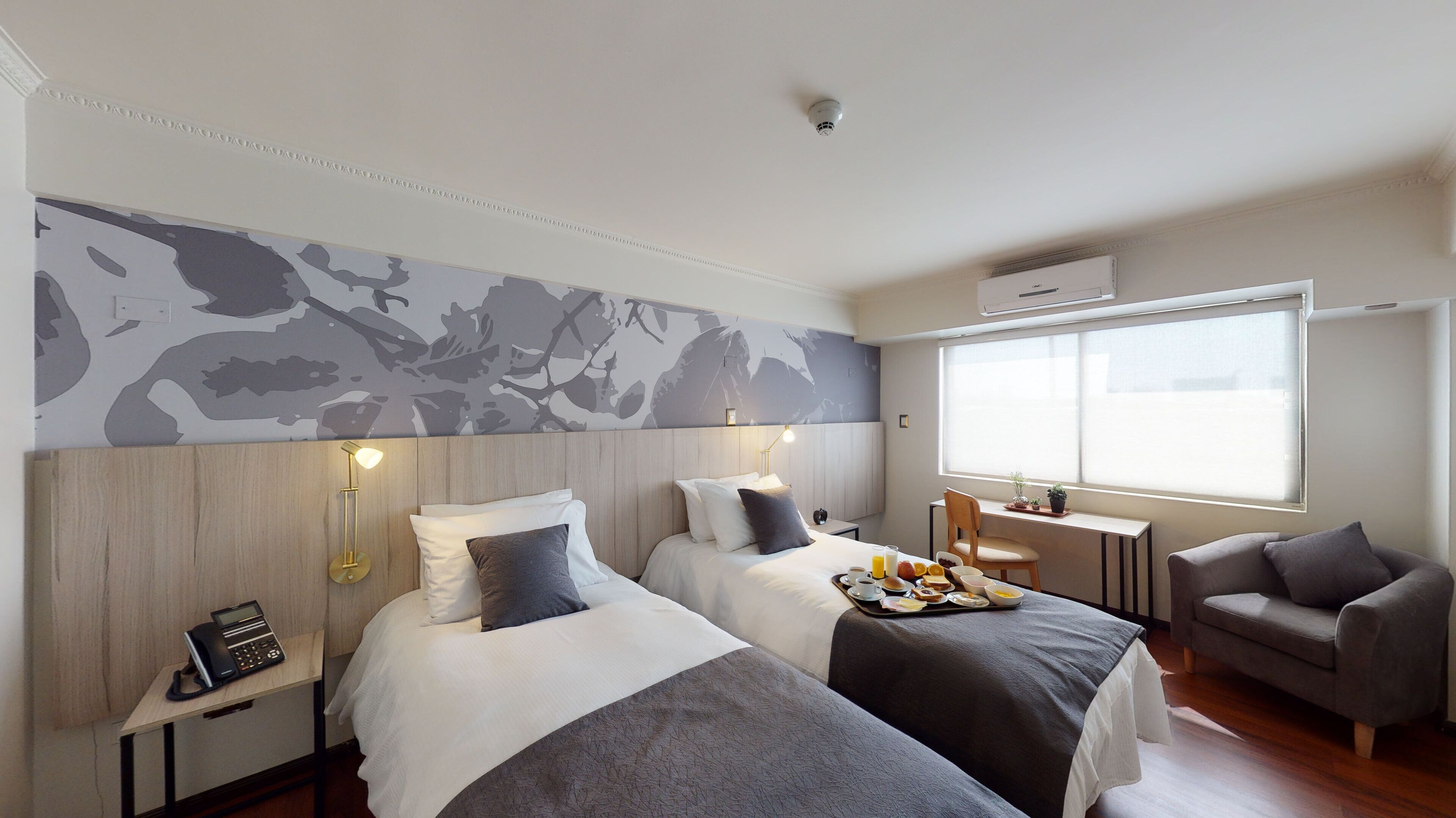 Habitación de hotel con dos camas, un escritorio con silla, una ventana con vistas y una cámara de seguridad instalada.
