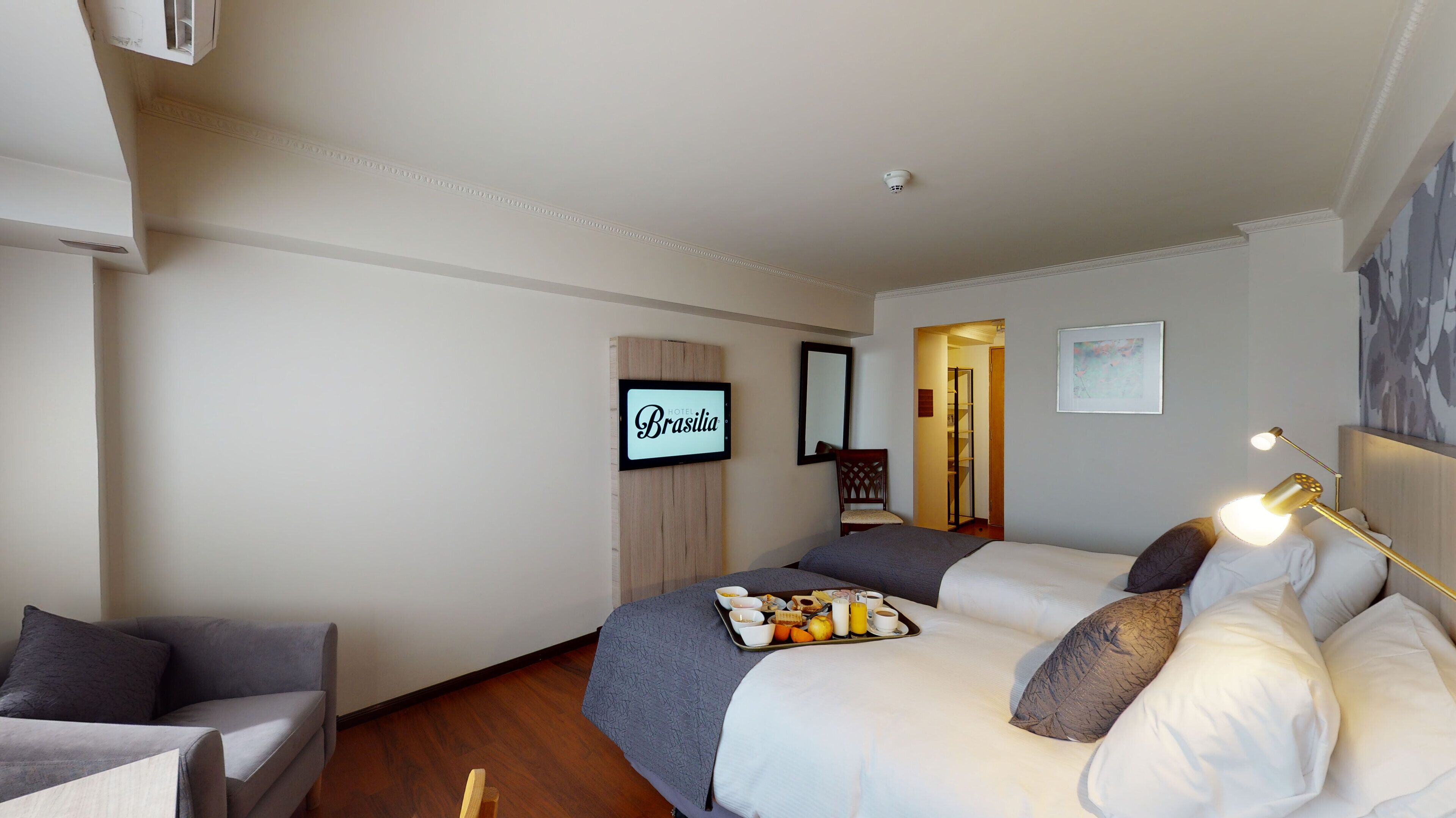 Et hotelværelse med en seng, et skrivebord, en stol, et bakke med morgenmad og et skilt der står "HOTEL Brasilia".