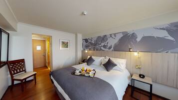 A hotel room with a bed, a chair, a tray of breakfast items, a nightstand with a lamp, and a wall with a floral mural.