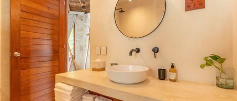 A bathroom with a wooden door, a round mirror, a white sink, and a shelf with towels.